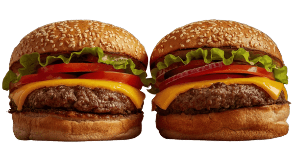 Two cheeseburgers side by side on a solid teal background, each with a sesame seed bun, beef patty, melted cheese, tomato slices, red onion, pickles, and leafy lettuce.